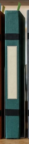 Digitally rendered: the spine of a dark teal green cloth notebook on a wooden shelf.