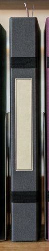 Digitally rendered: the spine of a charcoal gray cloth notebook on a wooden shelf.