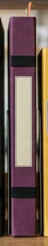 Digitally rendered: the spine of a plum cloth notebook on a wooden shelf.